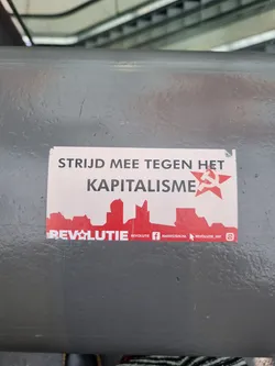 A sticker with a red star and a cityscape. The text on the sticker says "Fight with against capitalism" and has the name of a group called "Revolutie". There are also social media links to Facebook and Instagram.