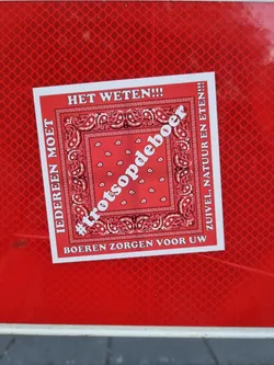 Street sticker A red sticker with a bandana-like design and the text '#trotsopdeboer' (proud of the farmer) in the center.  The text around it translates to: Everyone must know!!! Farmers provide your dairy, nature and food!!!