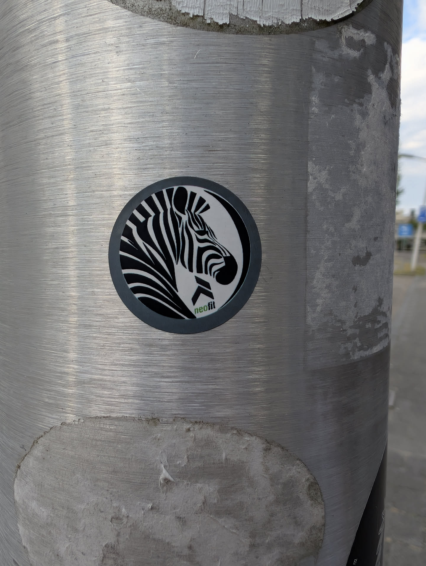 A round sticker on a metal pole showing a stylized black-and-white zebra profile. The text 'neofit' is printed in green and black at the bottom. The entire graphic is framed by a dark grey circular border.