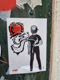 Street sticker This sticker features a stylized illustration of a boy in a cap carrying what seems to be a red heart-shaped object that's creating a flowing trail. The artwork is predominantly in black and red with a simple background.  The style is reminiscent of street art or graffiti.
