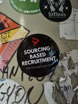 Street sticker A black round sticker with the text "SOURCING BASED RECRUITMENT" and the website frontwisegroup.com. The sticker has a red logo in the upper left corner.