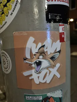 A sticker featuring a cartoon fox with the text 'Mad Fox'. The sticker is light brown with white lettering. 