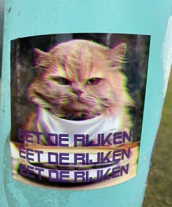 A sticker with a distorted image of an angry cat and the text 'eet de rijken' repeated three times. The text is Dutch for 'eat the rich'.
