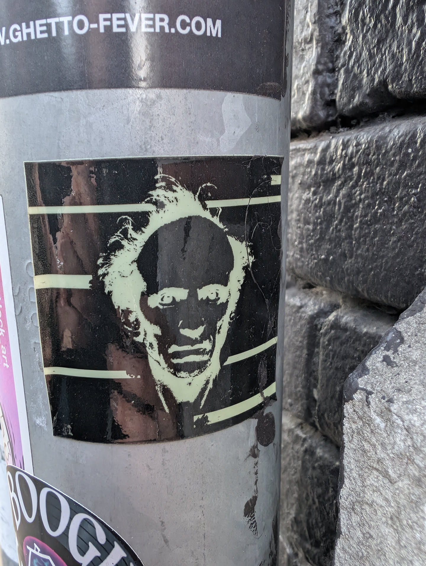 Square black sticker depicting a pale green stencil-style face with wild hair and a high forehead, set against horizontal background lines.