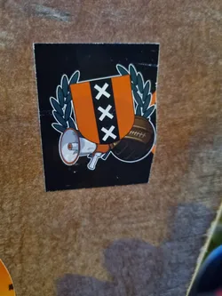 This sticker showcases the iconic Amsterdam coat of arms, three Xs on an orange background, surrounded by a laurel wreath.  It includes illustrations of a megaphone and a football, suggesting the theme of communication or supporting a football team. The sticker has a dark background, providing a strong contrast to the orange Amsterdam shield.