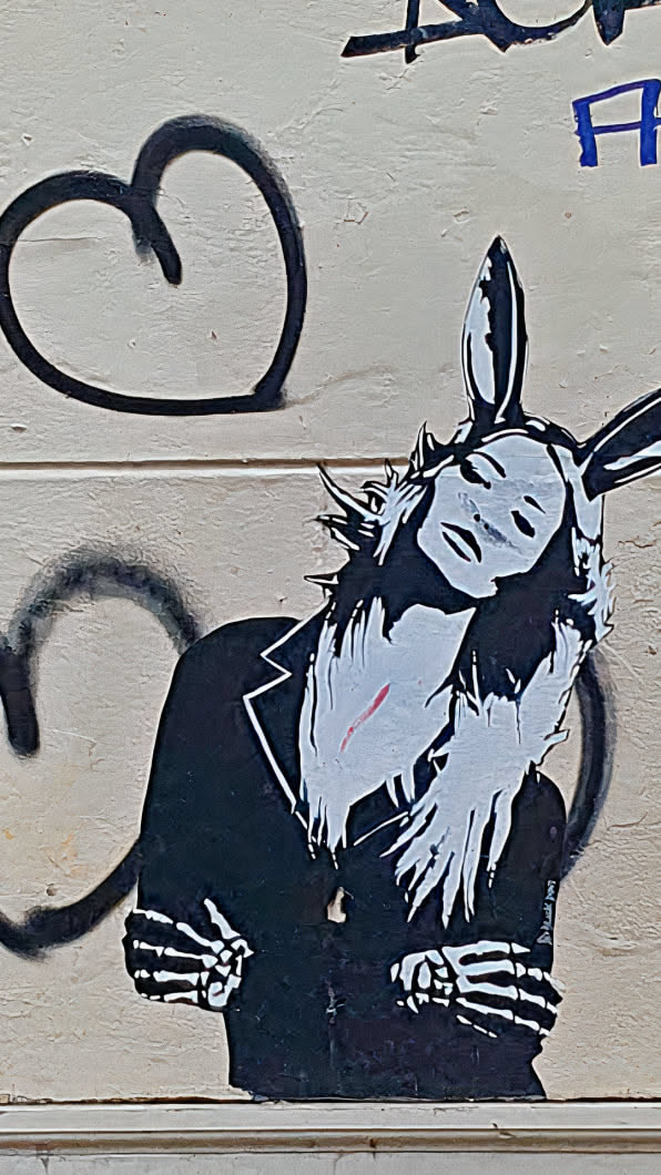 A black and white sticker features a striking visual of a rabbit-like character dressed in a suit with skeleton hands. The figure has long, spiky hair, giving it a punk or edgy look.