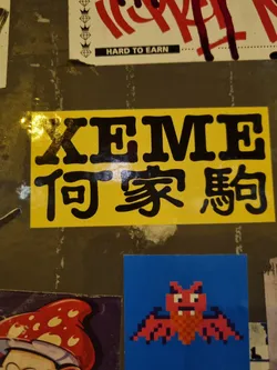 Street sticker A yellow sticker with black text. The text includes the English word "XEME" and Chinese characters that translate to "Ho Ka Ku." 