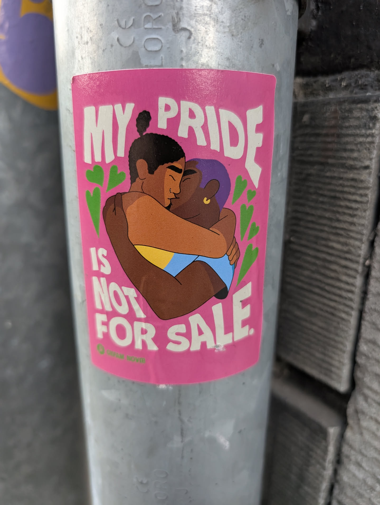 A pink rectangular sticker depicting two people of color kissing and hugging, flanked by green hearts. The text 'MY PRIDE IS NOT FOR SALE.' is written in bold white letters. A small green Oxfam Novib logo is at the bottom left.