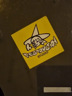 A yellow square sticker with a cartoon witch design and the text "Destruction Studio". The witch is depicted wearing a pointed hat and has a mischievous expression. The style is reminiscent of graffiti or street art.