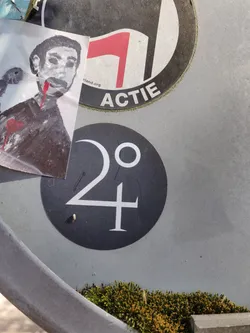 Street sticker A round black and white sticker with the number 24 and a degree symbol. It's simple yet intriguing.  There is another sticker nearby featuring a stylized image of a person, which may or may not be related.