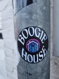 Round sticker imitating a vinyl record with the text "BOOGIE HOUSE" around a purple circle with a house icon inside. The house icon has blue lightning-like patterns inside.
