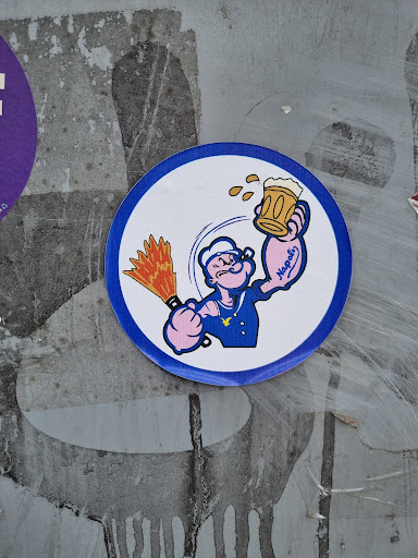 Round sticker featuring Popeye, the iconic sailor man, holding a beer mug and a flaming torch.  The sticker has a blue border and a white background. The style is reminiscent of classic Popeye cartoons.