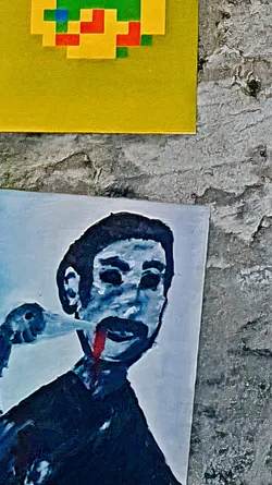 The sticker features a man rendered in a painterly style, with a stream of red coming from his mouth. The color palette is cool, with shades of blue and black contrasting with the splash of red. The overall effect is unsettling and thought-provoking. There's also a pixel art sticker above the portrait, featuring yellow, green and red colors.