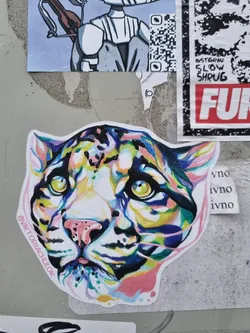 A vibrant and stylized sticker featuring the head of a clouded leopard. The artwork is done in a watercolor style with splashes of bright colors like pink, teal, yellow, and purple. The leopard's expression is calm and serene. The artist's Instagram handle is visible on the sticker.