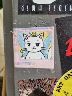 A sticker featuring a cute cartoon cat with fairy wings and a crown. The art style is reminiscent of early computer graphics or MS Paint. The cat holds a magic wand.