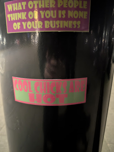 The image contains a close-up of a sticker on a trash can. The sticker is rectangular with green borders, with the words "COOL CHICKS ARE HOT" written in pink letters.