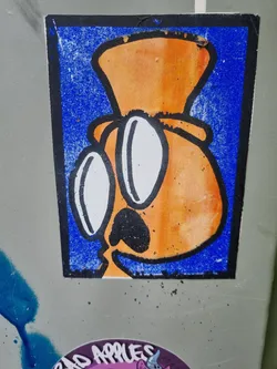 Street sticker A sticker featuring an orange cartoon character wearing a hat and glasses. The character has a simple design with a black nose and mouth. The background of the sticker is blue. 