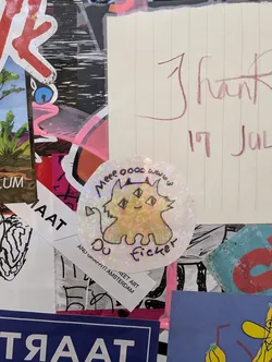 Holographic sticker of a cute three-eyed cat. The text on the sticker says "Meow 0000 www DU ficker". There is also text at the bottom that says GET ART ANL1 SH0PP1TT1 AMSTERDAM.