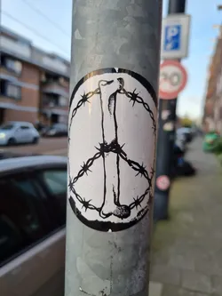 Street sticker This sticker displays a provocative image. A bone is placed inside a peace symbol, but the symbol's outline is made of barbed wire. This juxtaposition creates a strong visual statement on themes of peace and violence. The style is dark and slightly edgy.