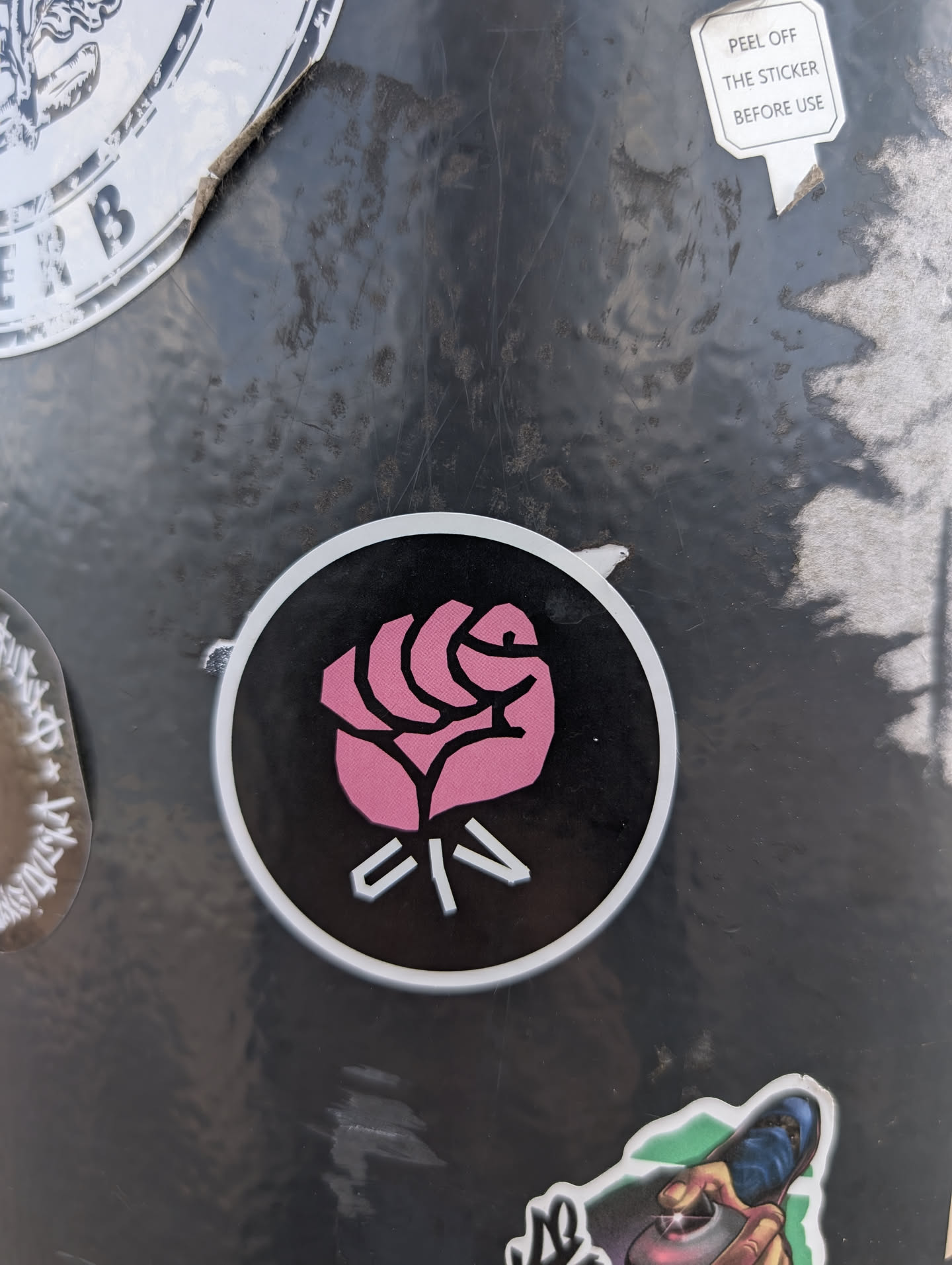 This is a round sticker featuring a pink rose with white accents on a black background. The design is simple and bold.