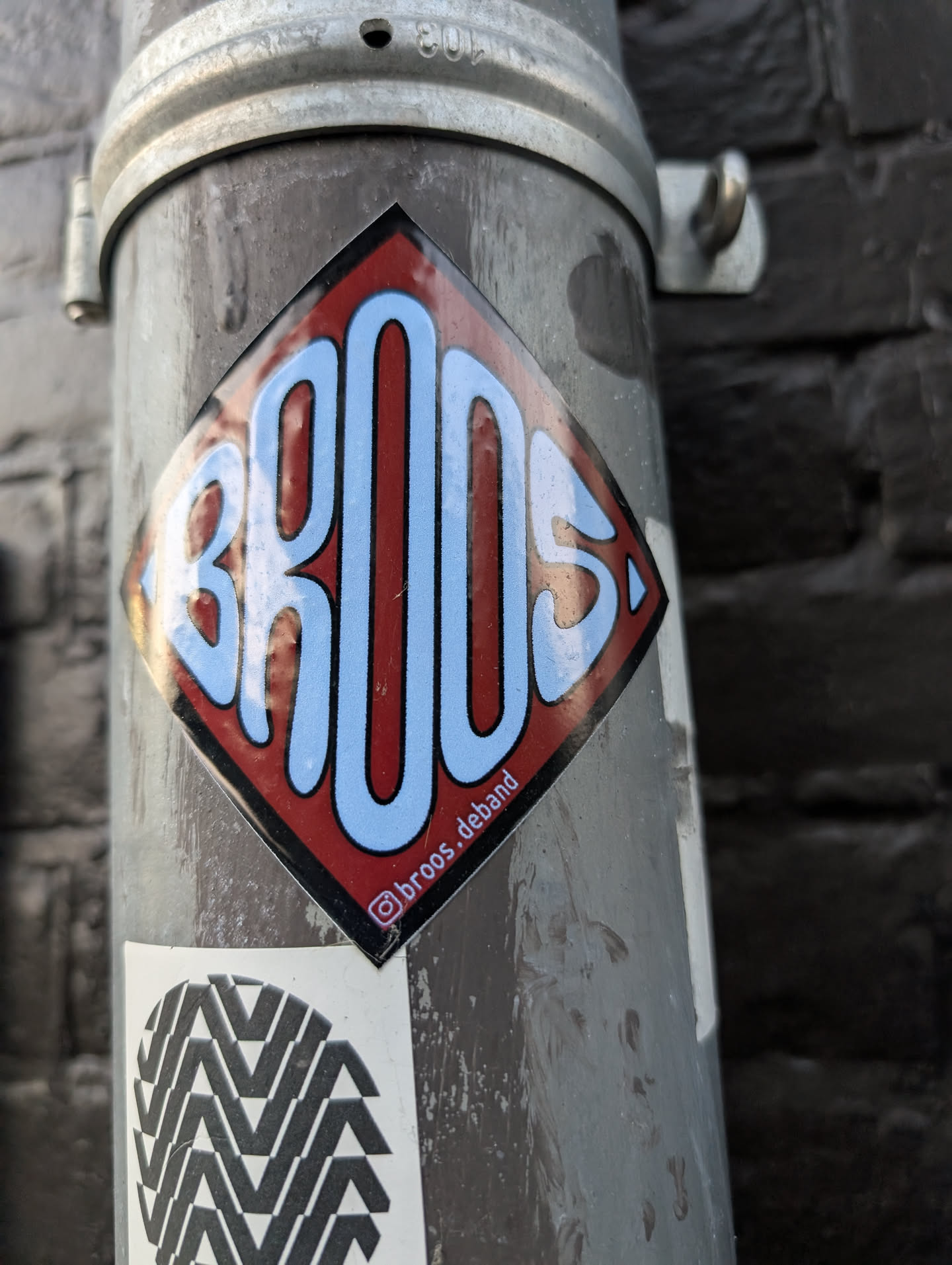 A diamond-shaped sticker with a black border, featuring the stylized word 'BROOS' in light blue bubble letters on a red background. Includes a small Instagram handle along the bottom right edge.