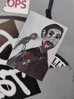 Street sticker A sticker with a dark, slightly gory illustration of a man with a bird seemingly sucking his blood. The style is reminiscent of dark art or surrealism.  The sticker is rectangular and printed on what appears to be matte sticker paper.