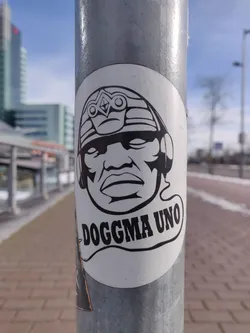 Black and white sticker featuring a stylized illustration of a person wearing a helmet and headphones. The text 'DOGGMA UNO' is written below the illustration. 