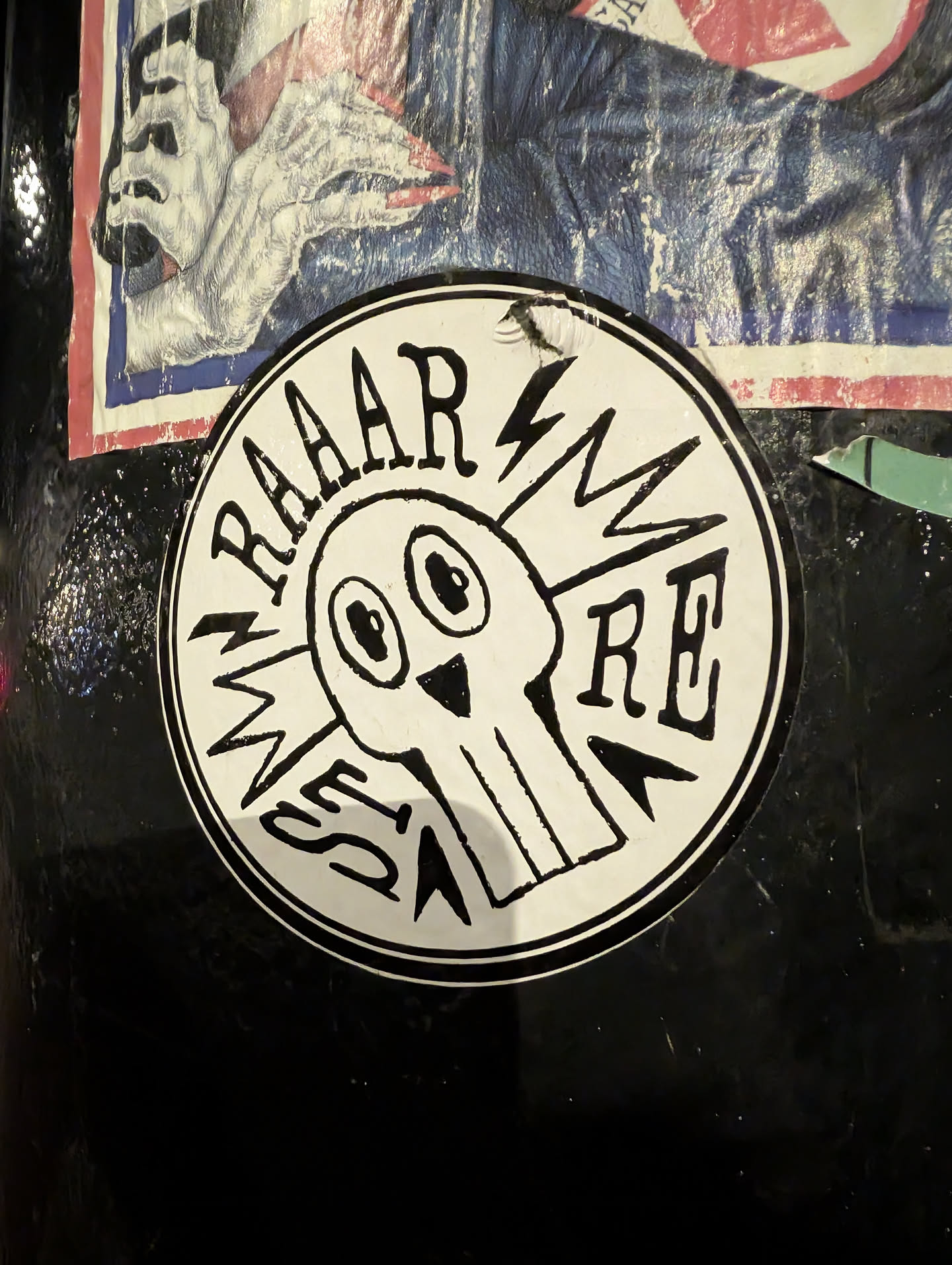 Street sticker A circular, black and white sticker featuring a stylized, cartoonish skull or monster head at its center. The head has large, wide-set black eyes and a small, inverted triangular nose. Lightning bolt shapes emanate from the sides of the head. Arched over the top of the head are the letters 'RAAAR'. On the left side, vertically oriented, are the letters 'MESS', and on the right side, horizontally, are the letters 'RE'. The entire design is rendered in a thick, hand-drawn, somewhat crude style with a black outline and details on a white background.