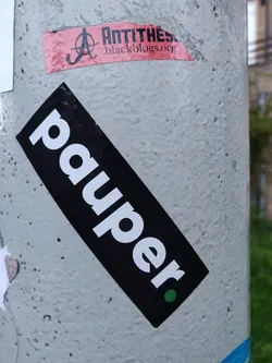 A black and white sticker with the word "pauper" written in a bold, sans-serif font. There's a small green dot at the bottom right corner of the sticker.