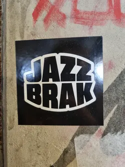 A black and white sticker with the words JAZZ BRAK in a stylized font. The text is bold and set within a circular shape.  The sticker has a glossy finish.