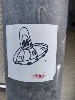 Street sticker A white sticker with a black and white illustration of a cartoon UFO. The UFO has a rounded top with two small circles that look like eyes and rivets along its body. The sticker has the word "Ghost" written underneath in red.