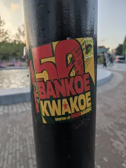 Street sticker A rectangular sticker featuring a red, yellow, and green color scheme. It displays a large red '50' alongside the bold text 'BANKOE KWAKOE'. The top-right corner mimics a Surinamese immigration stamp and postage stamp, while additional text borders the left and bottom edges.