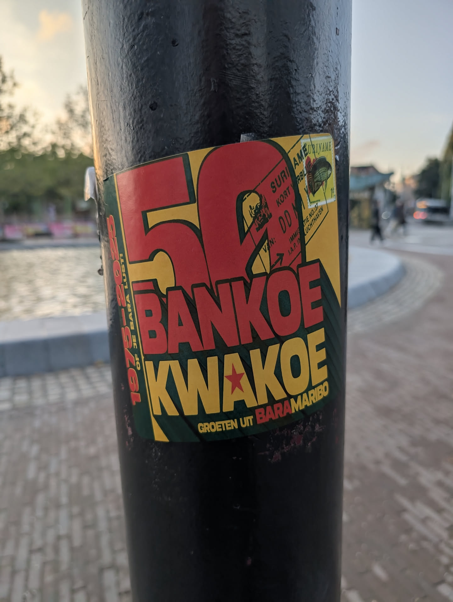 A rectangular sticker featuring a red, yellow, and green color scheme. It displays a large red '50' alongside the bold text 'BANKOE KWAKOE'. The top-right corner mimics a Surinamese immigration stamp and postage stamp, while additional text borders the left and bottom edges.