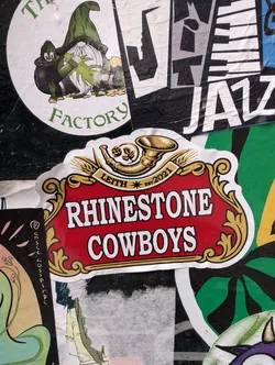 A rectangular sticker with a red background and ornate gold border. The sticker reads 'RHINESTONE COWBOYS' and 'LEITH EST. 2021' with a logo of a horn above the text.