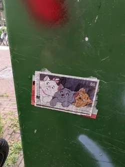 Street sticker The sticker features three cartoon cats with distinct colors and expressions, positioned side-by-side. The leftmost cat is white with a pink bow and collar. The middle cat is grey with a grey collar. The rightmost cat is orange-brown with a red bow. They are all depicted with large eyes and a slightly melancholic expression. The background of the sticker is a faded greyish-white, with what appears to be printed lines. In the upper right corner of the sticker, the number '66' is visible in black. The sticker has a slightly worn appearance and is attached to a green surface with some peeling edges, suggesting it has been adhered for some time.