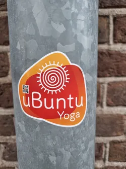 Street sticker A red and orange sticker with the text "uBuntu Yoga" and an illustration of a sun with a spiral in the center.  There is a small QR code in the upper left corner of the sticker.