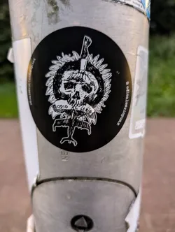 This sticker features a striking graphic design. A skull is depicted centrally, pierced by a knife, encompassed by a stylized sun or floral burst. The phrase "ODIO EL LENIO" is visible beneath the skull, suggesting a message or title. The overall style is minimalist and dark, typical of underground or alternative art.