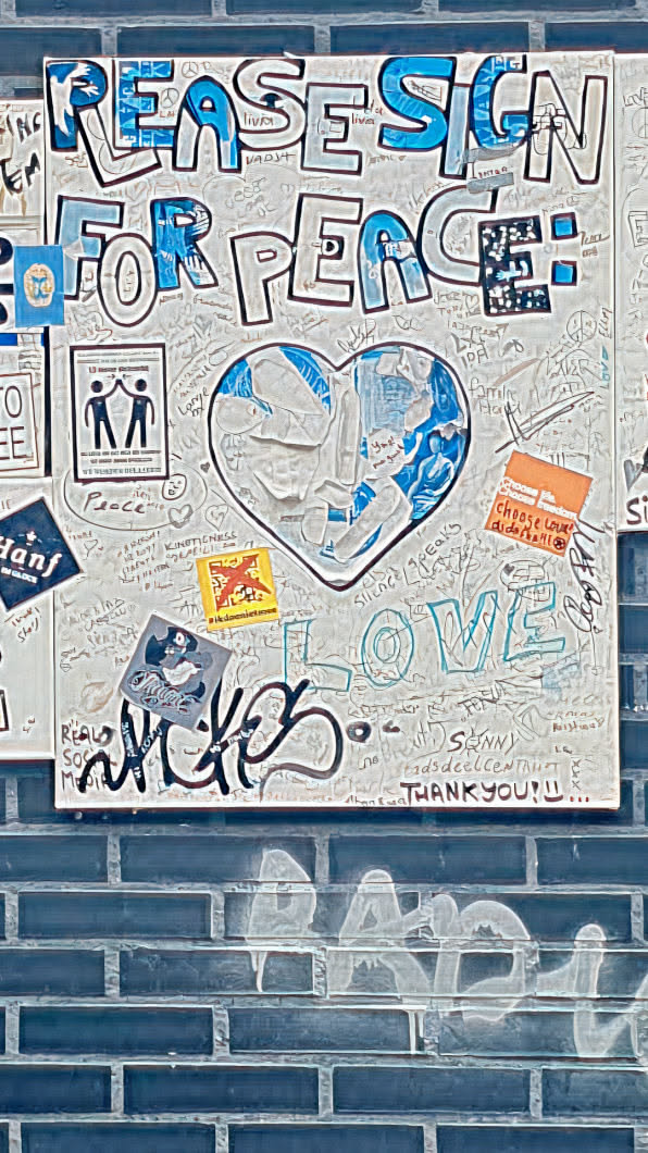 This board is filled with various stickers, drawings, and handwritten messages, all centered around the themes of peace, love, and social activism. Notable elements include a heart design filled with blue imagery, the word "LOVE" written prominently, and various calls for peace.
