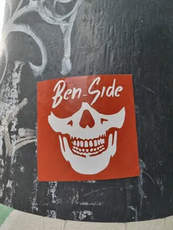 An orange sticker with a white skull wearing sunglasses. The text 'Ben-Side' is written at the top.