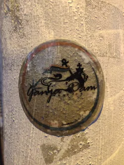 Street sticker A round sticker featuring a design that includes a lion, a banner, and an anchor. The text "Ganja Dam" is prominently displayed, along with the words "imokersclub" at the bottom. The sticker appears to be weathered and slightly worn, giving it a vintage feel. 