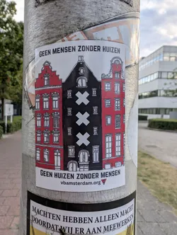 Street sticker A rectangular sticker depicting three Amsterdam canal houses. The central house is black with three vertical white crosses, flanked by two red houses. Bold Dutch text is printed at the top and bottom, with a website URL at the base.