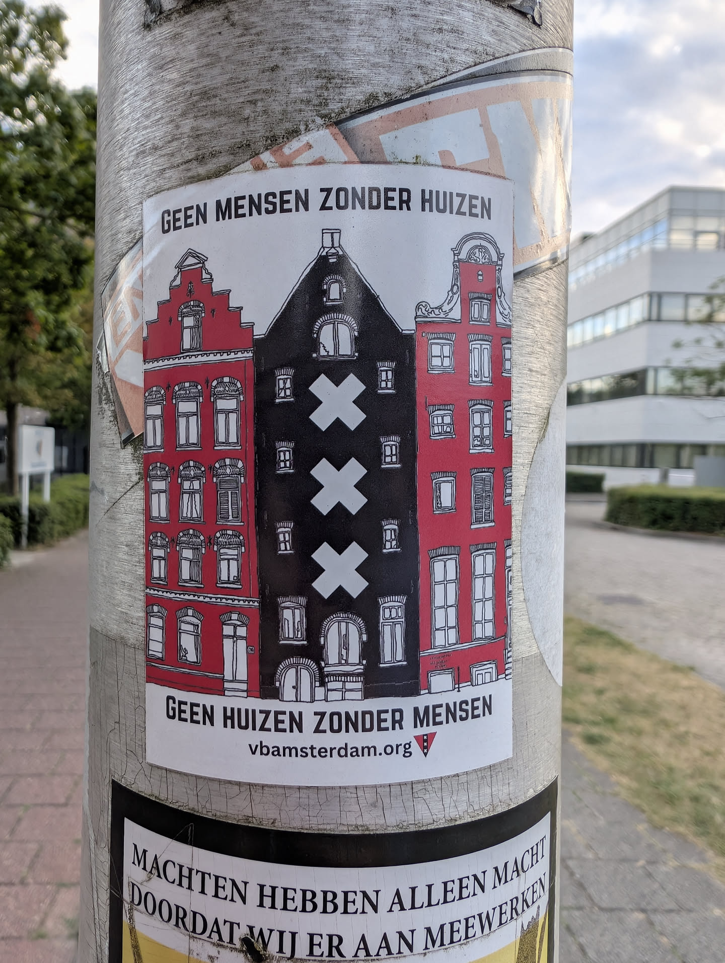 A rectangular sticker depicting three Amsterdam canal houses. The central house is black with three vertical white crosses, flanked by two red houses. Bold Dutch text is printed at the top and bottom, with a website URL at the base.