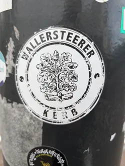 Street sticker Black and white sticker with a circular design. It features an oak tree emblem in the center, surrounded by text that reads "WALLERSTEERER" at the top and "KERB" at the bottom. The style is simple and classic, possibly representing a local event or community.