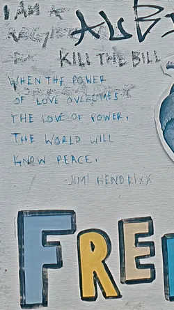 Street sticker The image shows a section of a painted wall. It features various texts, including 'KILL THE BILL,' a quote from Jimi Hendrix: 'WHEN THE POWER OF LOVE OVERCOMES THE LOVE OF POWER, THE WORLD WILL KNOW PEACE.' There's also a large painted word, 'FREE,' with each letter in a different color.