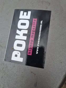 A black and white sticker with the text POKOE in large white letters,  the words "hiphop magazine" written in smaller pink letters and website address www.pokoemagazine.nl at the bottom. 