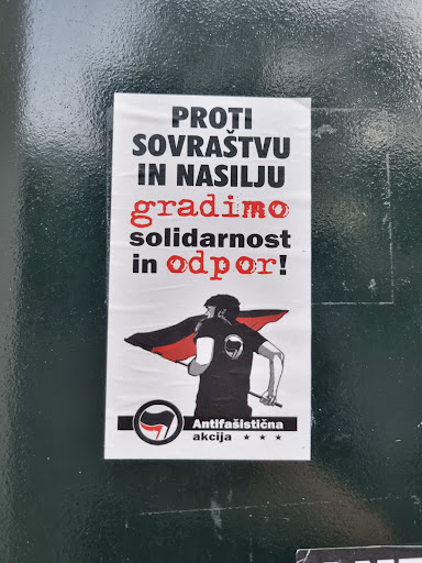 Street sticker A sticker with an illustration of a person holding a black and red flag. The text on the sticker is in Slovenian and translates to "Against hatred and violence, we build solidarity and resistance!"