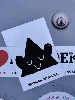 Street sticker A white square sticker with a minimalist design of a black triangle character. The character has a simple face with closed eyes and a small smile. The website www.baskosters.com is printed at the bottom of the sticker. 