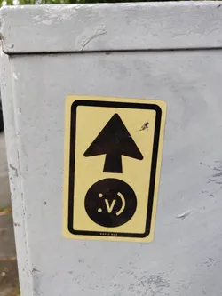 Street sticker A yellow sticker with a black upward arrow and a smiley face with a V-shaped mouth.  The text "RAPID WAX" is visible at the bottom.