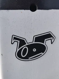 Street sticker A black and white sticker featuring a stylized cartoon character with large ears and a simple face. The character's design is minimalist and geometric. The sticker is affixed to a light gray surface.
