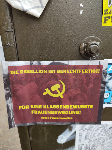 Street sticker A sticker featuring a hammer and sickle, along with the text "Die Rebellion ist gerechtfertigt!" ("The rebellion is justified!") and "Für eine klassenbewusste Frauenbewegung!" ("For a class-conscious women's movement!"). The sticker also includes the name "Rotes Frauenkomitee" (Red Women's Committee).